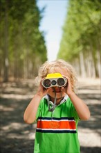 Boy (2-3) looking through binoculars in tree farm.