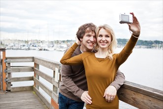 USA, Washington, Seattle, Young couple taking photos on pier. Photo: Take A Pix Media