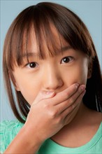 Studio shot of girl (10-11) covering mouth with hand. Photo: Rob Lewine