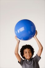 Studio portrait of boy (8-9) holding blue ball. Photo : Rob Lewine