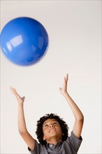 Studio shot of boy (8-9) tossing blue ball. Photo : Rob Lewine