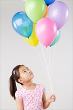 Studio shot of girl (8-9) holding bunch of balloons. Photo : Rob Lewine