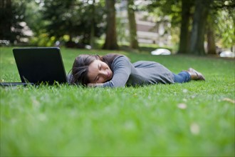 Young woman lying on grass using laptop. Photo : Jan Scherders