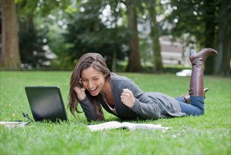 Young woman lying on grass using laptop and cell phone. Photo : Jan Scherders