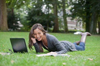 Young woman lying on grass using laptop and cell phone. Photo: Jan Scherders