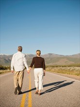 Mid adult couple walking along empty road . Photo: Erik Isakson