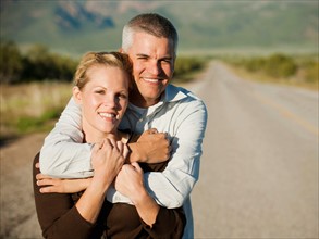 Mid adult couple embracing on empty road. Photo: Erik Isakson