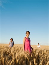 Girls (10-11, 12-13) and boy (8-9) standing in wheat field.