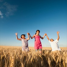 Girls (10-11, 12-13) and boy (8-9) walking though wheat field.