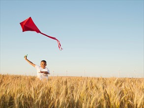 Boy (10-11) playing with kite in wheat field.