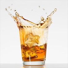 Studio shot of ice cubes splashing into glass of whiskey.