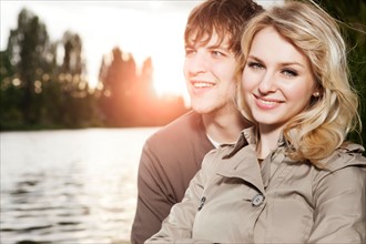 Portrait of young couple embracing by lake at sunset. Photo : Take A Pix Media