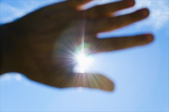 Close up of hand against blue sky with sun beams.