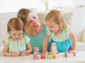 Mother and daughters (2-3) playing with letter blocks.