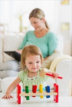 Girl (2-3) playing in living room, mother in background.