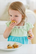 Girl (2-3) eating muffins.