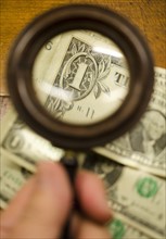 Hand holding magnifying glass over dollar bills, studio shot.