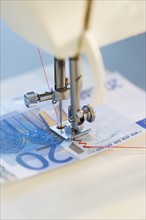 Sewing machine stitching 20 euro note, studio shot.