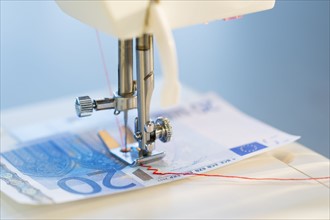 Sewing machine stitching 20 euro note, studio shot.