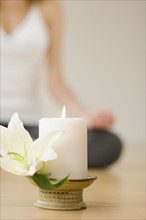 Candle and flower with woman practicing yoga in background, studio shot.