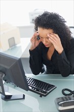 Business woman using computer holding head in hands.