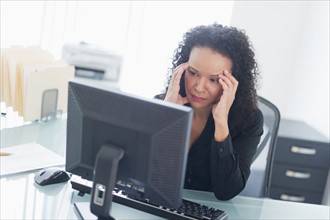 Business woman using computer holding head in hands.