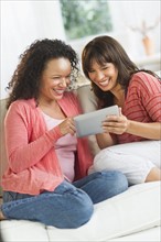 Two women sitting on sofa using digital tablets.