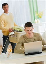 Son (16-17) using laptop being observed by father.