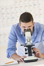 Teenage student (16-17) looking through microscope.