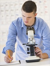Teenage student (16-17) with microscope doing notes.