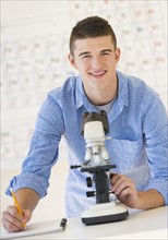 Teenage student (16-17) with microscope doing notes.