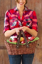 Smiling woman holding basket full of apples.