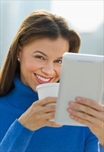 Woman working on digital tablet and drinking coffee.