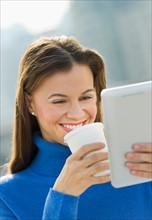 Woman using digital tablet and drinking coffee outdoors.