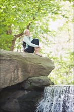 USA, New York, New York City, Manhattan, Central Park, Young woman sitting on rock. Photo: Daniel