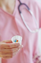 Close up of hand of female nurse holding cup with pills. Photo: Daniel Grill