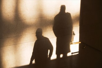 Shadow of two male pedestrians on sunlit wall. Photo : fotog