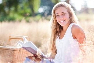 Teenage girl (16-17) posing for portrait while reading book outdoors. Photo: Take A Pix Media