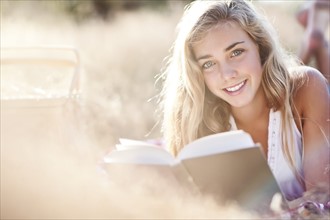Teenage girl (16-17) posing for portrait while reading book outdoors. Photo: Take A Pix Media