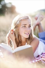 Teenage girl (16-17) taking break from reading book outdoors. Photo : Take A Pix Media