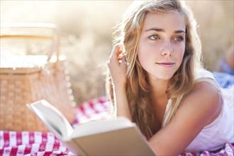 Teenage girl (16-17) taking break from reading book outdoors. Photo: Take A Pix Media