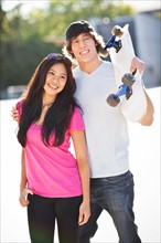 Young multi-racial couple posing with skateboard. Photo : Take A Pix Media