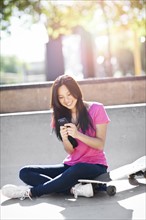 Young chinese woman text messaging while sitting on skateboard. Photo: Take A Pix Media