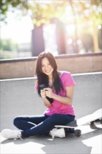 Young chinese woman text messaging while sitting on skateboard. Photo: Take A Pix Media