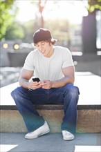 Young man sitting outdoors, text messaging. Photo : Take A Pix Media