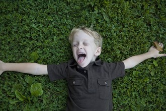Boy (4-5) lying on lawn laughing. Photo : Johannes Kroemer