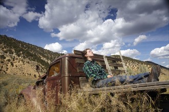 USA, Colorado, Woman resting on bed of abandoned truck in desert. Photo: John Kelly