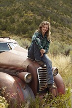 USA, Colorado, Portrait of woman resting on abandoned truck in desert. Photo: John Kelly