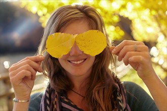 Woman covering eyes with autumn leaves. Photo : John Kelly