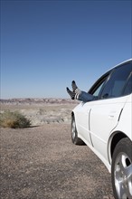 USA, Arizona, Winslow, Woman sticking feet out of car window parked in desert. Photo: Winslow
